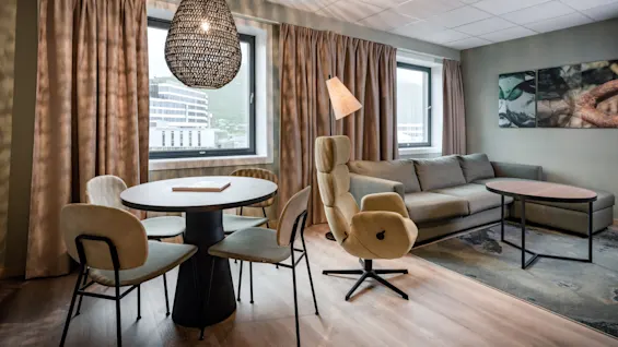 A stylish hotel room offering a cozy living space with a sofa and armchair, alongside a dining area for meals or work.