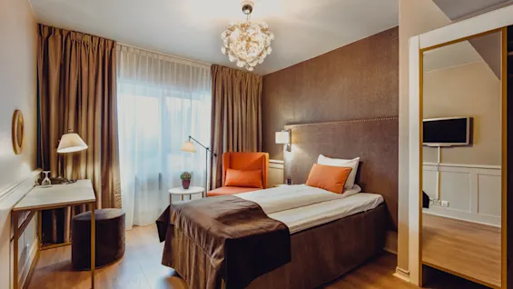 Elegant bedroom with a neatly made bed, furniture, and a glowing chandelier, conveying warmth and comfort.