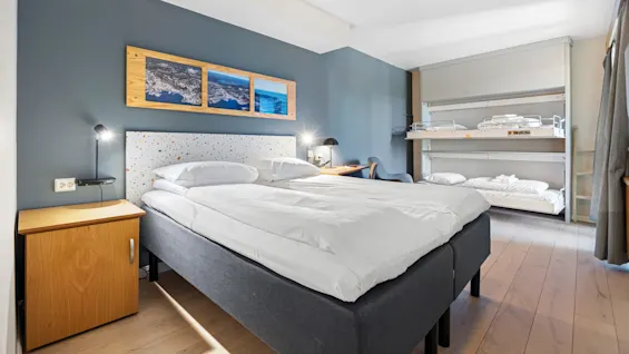 A neatly made double bed centers a modern bedroom with blue walls, wooden furniture, decorative pillows, and art above the headboard.