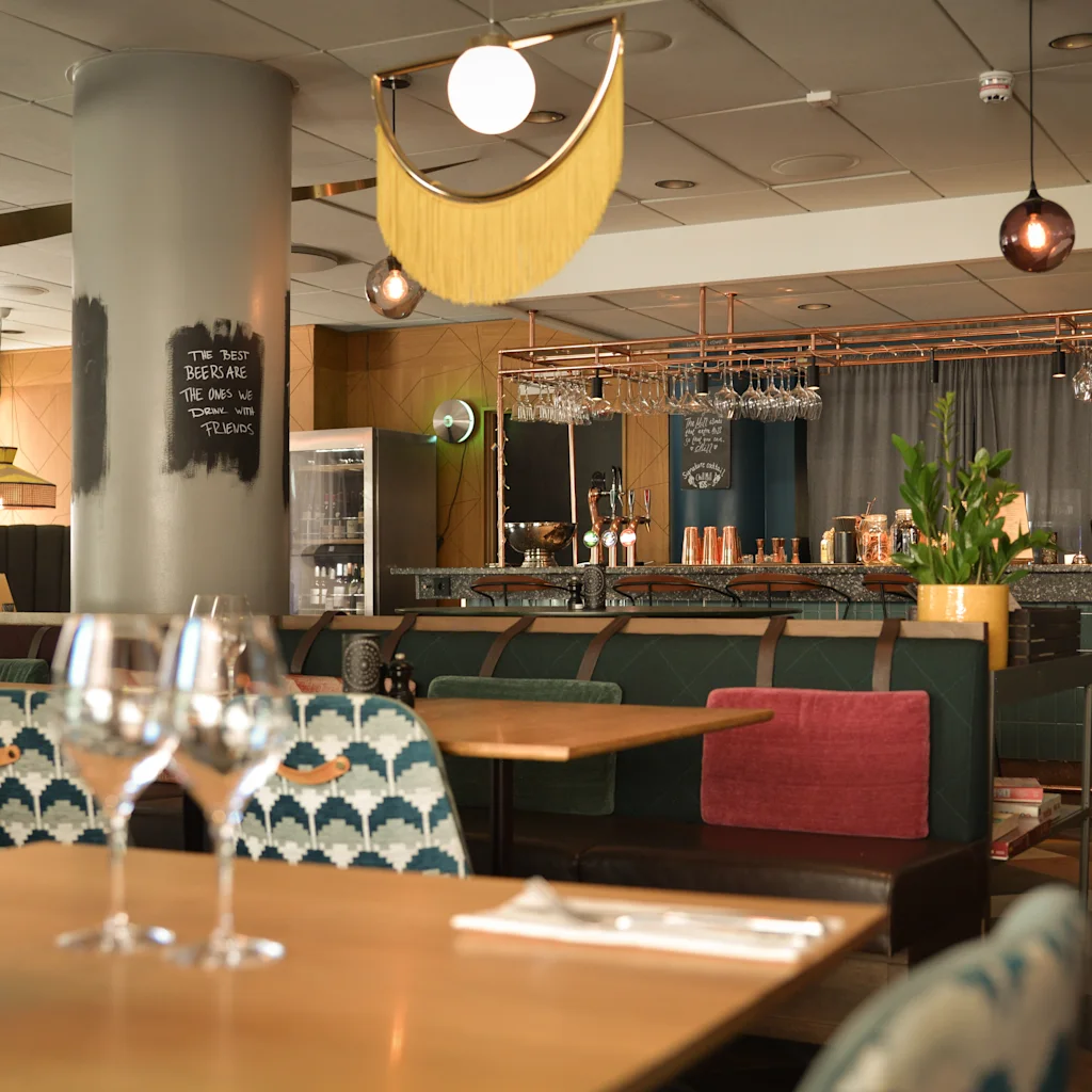 En stilfull restaurang- eller barinteriör med dukade bord, ett framträdande barområde och dekorativ belysning. Baren är öppen till sent.