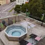 Rooftop terrace with a bubbling hot tub, lounge chairs, and wicker seating, offering a view of the city below.
