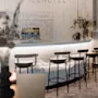 En buet bardisk viser stole og glas i et minimalistisk rum med blød belysning. "ICEHOTEL"-tekst er monteret på væggen blandt hængende dekorationer.