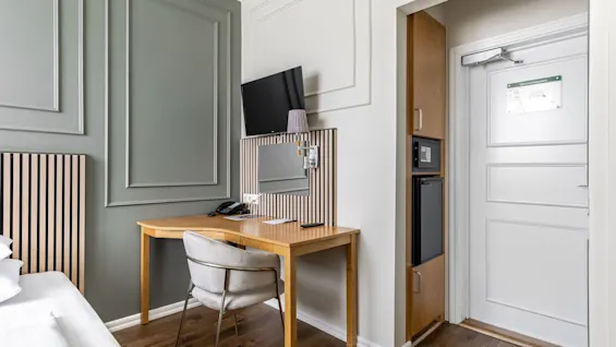 Viihtyisä hotellihuone Comfort Hotel Linköping Cityssä, jossa on työpöytä, tuoli, TV ja minibaari, täydellinen työhön tai rentoutumiseen.