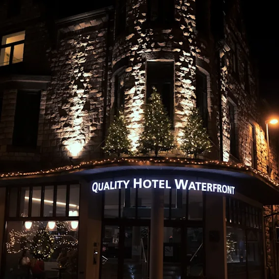 Quality Hotel Waterfront i Ålesund om natten med varm fasadebelysning og belyste juletrær over inngangen.