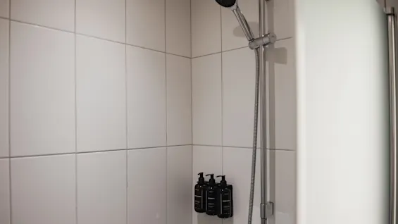 Duschutrymme på Home Hotel Grand, Helsingborg, med vita kakelplattor, duschhuvud och dispensrar för schampo, balsam, kroppstvål.