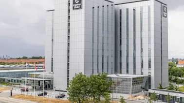 Korkea, moderni rakennus merkittynä “Clarion Hotel” suurilla lasi-ikkunoilla seisoo kaupunkiympäristössä. Liput liehuvat sisäänkäynnin lähellä.