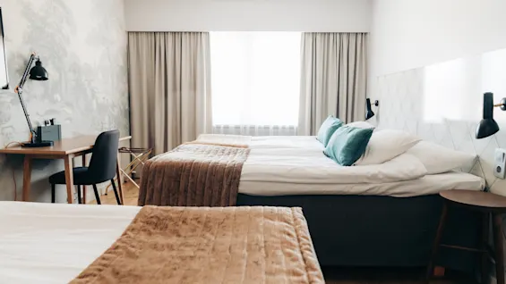 Bright hotel room with comfortable beds, a wooden desk, and soft natural light coming through the window.