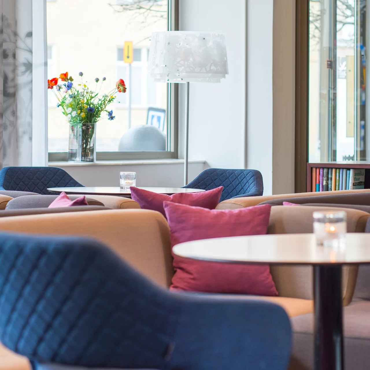 Komfortabel sittegruppe i et moderne oppholdsrom med blå og beige stoler, lilla puter og et bord, omgitt av store vinduer og en vase med fargerike blomster.