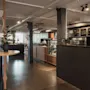 Moderni ja kutsuva hotelliravintola tai baarialue tummalla tiskillä, puupöydillä ja viherkasveilla avoimessa tilassa.