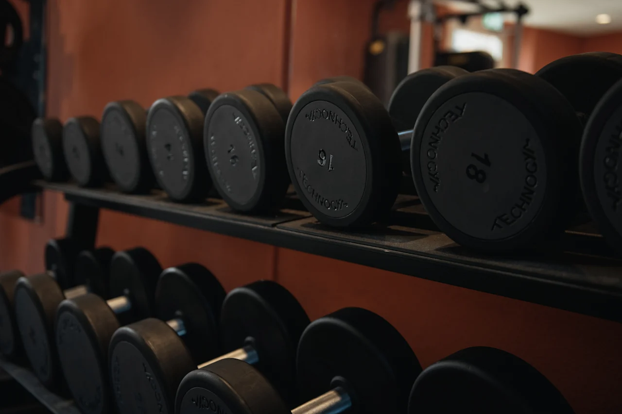 Et stativ med håndvægte i et fitnesscenter, med vægtene 16 og 18 synlige, klar til en træning.