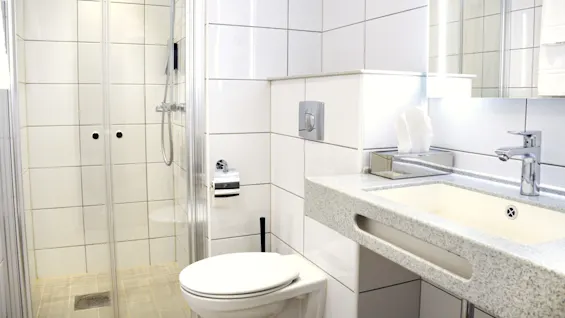 Et moderne badeværelse med en gå-ind brusekabine, toilet og vask mod flisebelagte vægge.