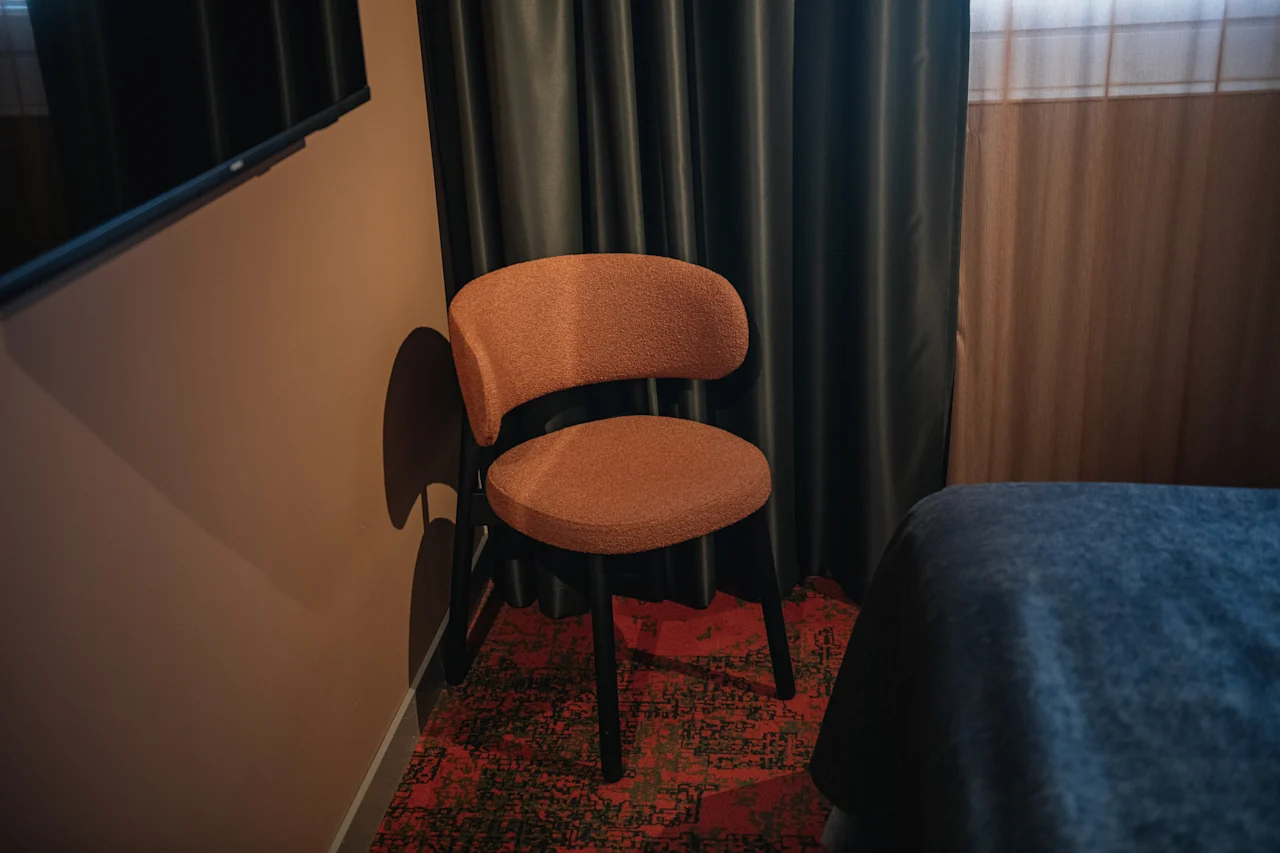 Et komfortabelt hotellrom med en stilig stol, en pent oppredd seng og mørke gardiner, som antyder et avslappende opphold.
