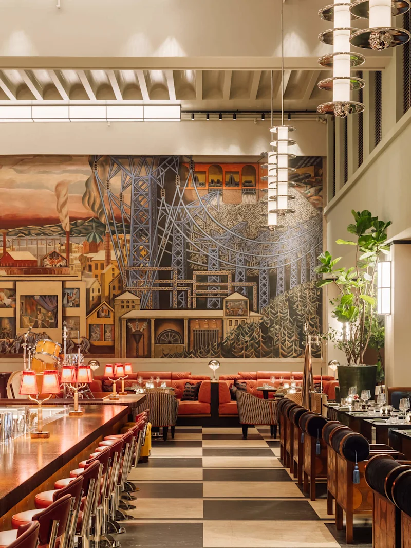 Tyylikäs sisustus suurella seinämaalauksella, art deco -valaistuksella ja ylellisillä istuimilla korkeassa huoneessa.