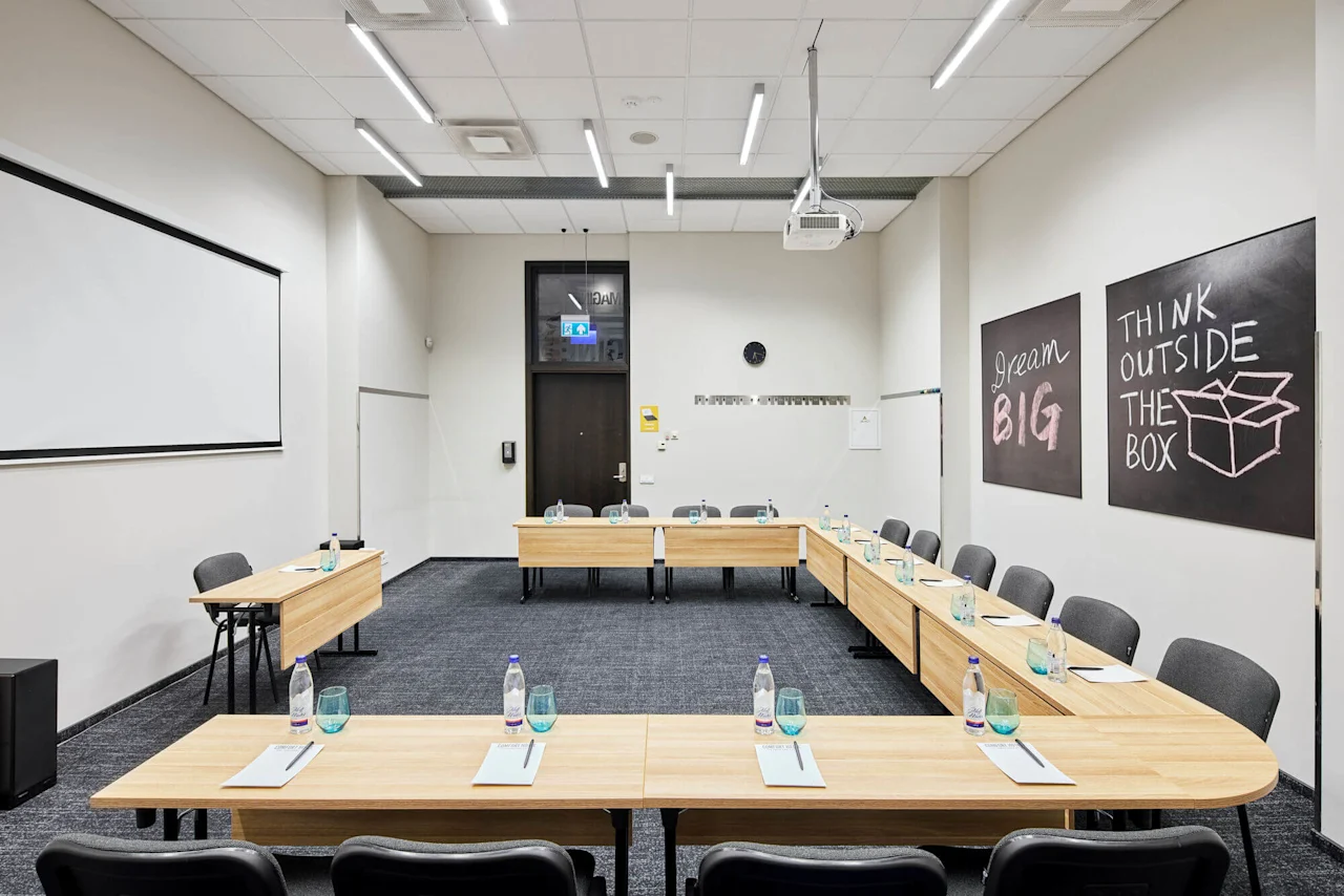 Meeting room with U-shaped wooden tables set with notepads and water bottles. Two chalkboards display "Dream BIG" and "THINK OUTSIDE THE BOX." Projector and screen installed overhead. 