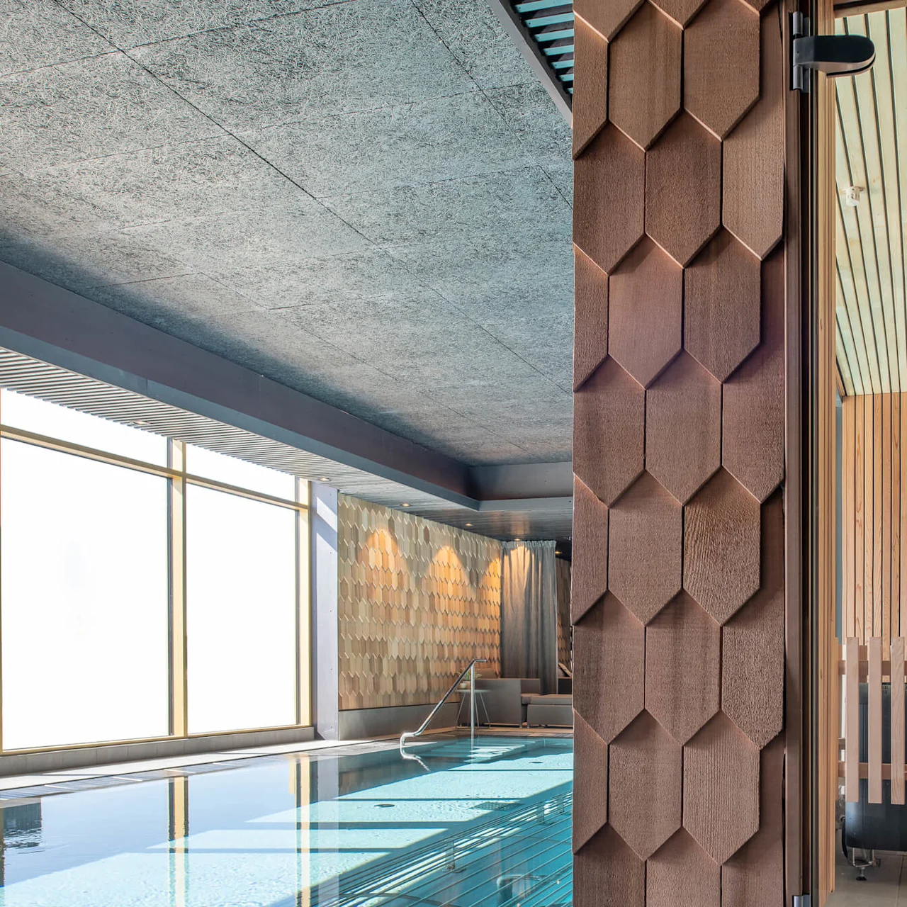 A pool reflects light, adjacent to a sauna room lined with wooden panels. The setting is modern and luxurious, featuring geometric wall patterns and large windows.