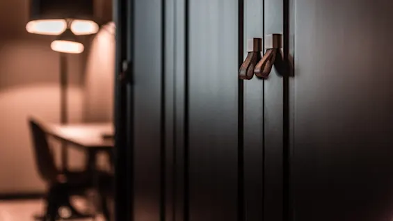 Dark cabinet doors with leather handles stand in sharp focus, contrasted by a softly lit workspace featuring a blurred desk and lamp in the background.