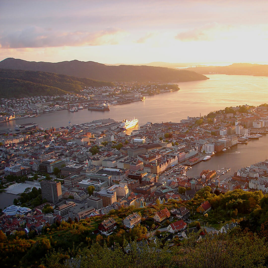 Utsikt från en bergssida över norska staden Bergen i solnedgång.