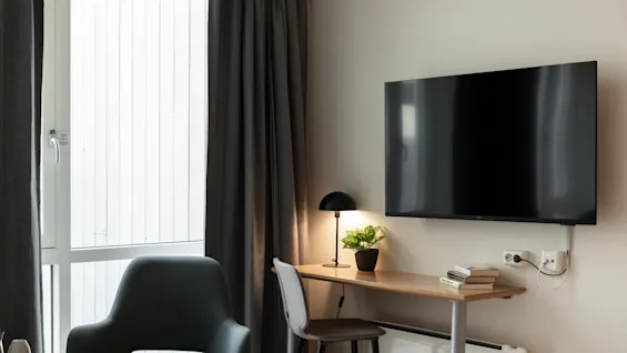 An inviting hotel room featuring a comfortable workspace with a lamp, books, and a television for entertainment.