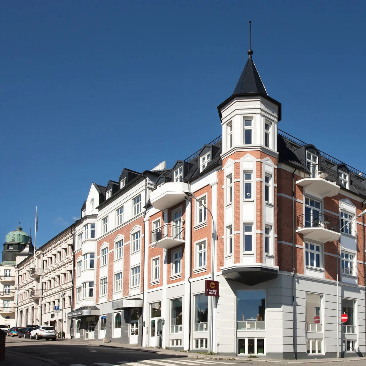 Ett hörnhus med torn, balkonger och stora fönster under en klarblå himmel.
