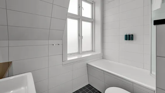 Ett modernt badrum med vita kaklade väggar, fönster, badkar och minimalistiska hyllor.