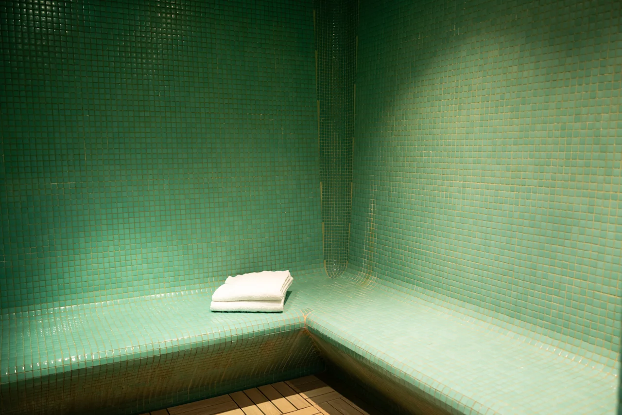 Grönt kaklat ångbad med en böjd bänk och en prydligt vikt vit handduk, inbjudande till avkoppling.