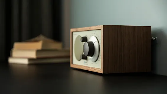 En radio i vintagestil med trekabinett står på en mørk overflate, med uskarpe bøker i bakgrunnen.