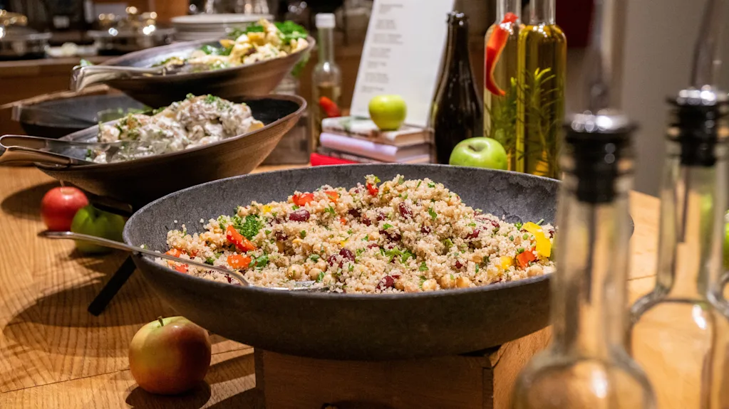 Colorful quinoa salad in a large bowl at a buffet with oils and apples in the background.