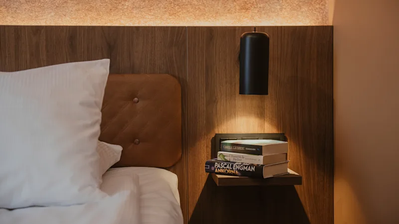 En hyggelig sengeplads med bøger inklusive Pascal Engman Ankorna på en hylde, oplyst af en væglampe, ved siden af en seng.