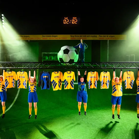 Fotbollsspelare som hänger från en metallbjälke på en scen med tröjor hängande runt sig under strålkastare