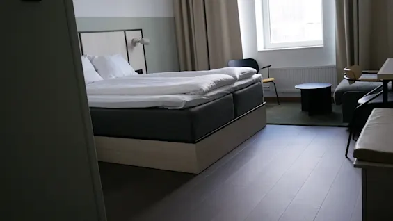 A modern hotel room at Comfort Hotel Norrköping with a neatly made bed, a window with curtains, and a small seating area. Room number 21 is visible.