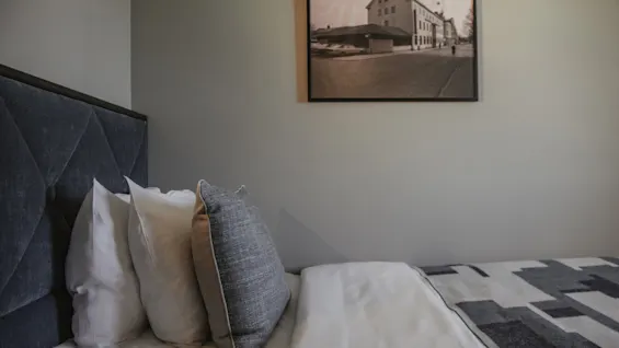 Ett hotellrum med en bekväm säng, mörk sänggavel och kuddar. En inramad svartvit bild av en gatuscen hänger på väggen.