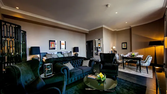 Luksuriøst oppholdsrom med komfortable sorte møbler, et glassbord og elegant dekor. Et formelt spiseområde med dekket bord er plassert nær et stort vindu, noe som forsterker den koselige atmosfæren.