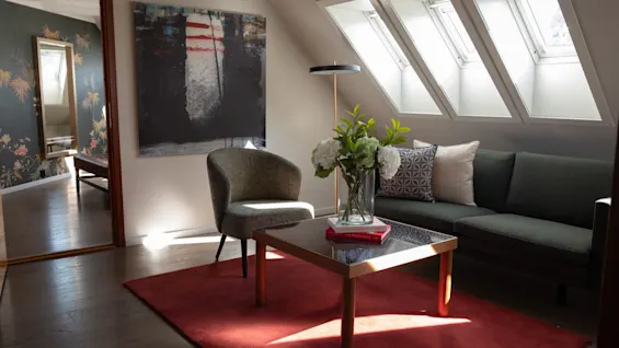 En koselig stue med en mørkegrønn sofa, en lenestol, et salongbord og tre lyse takvinduer.