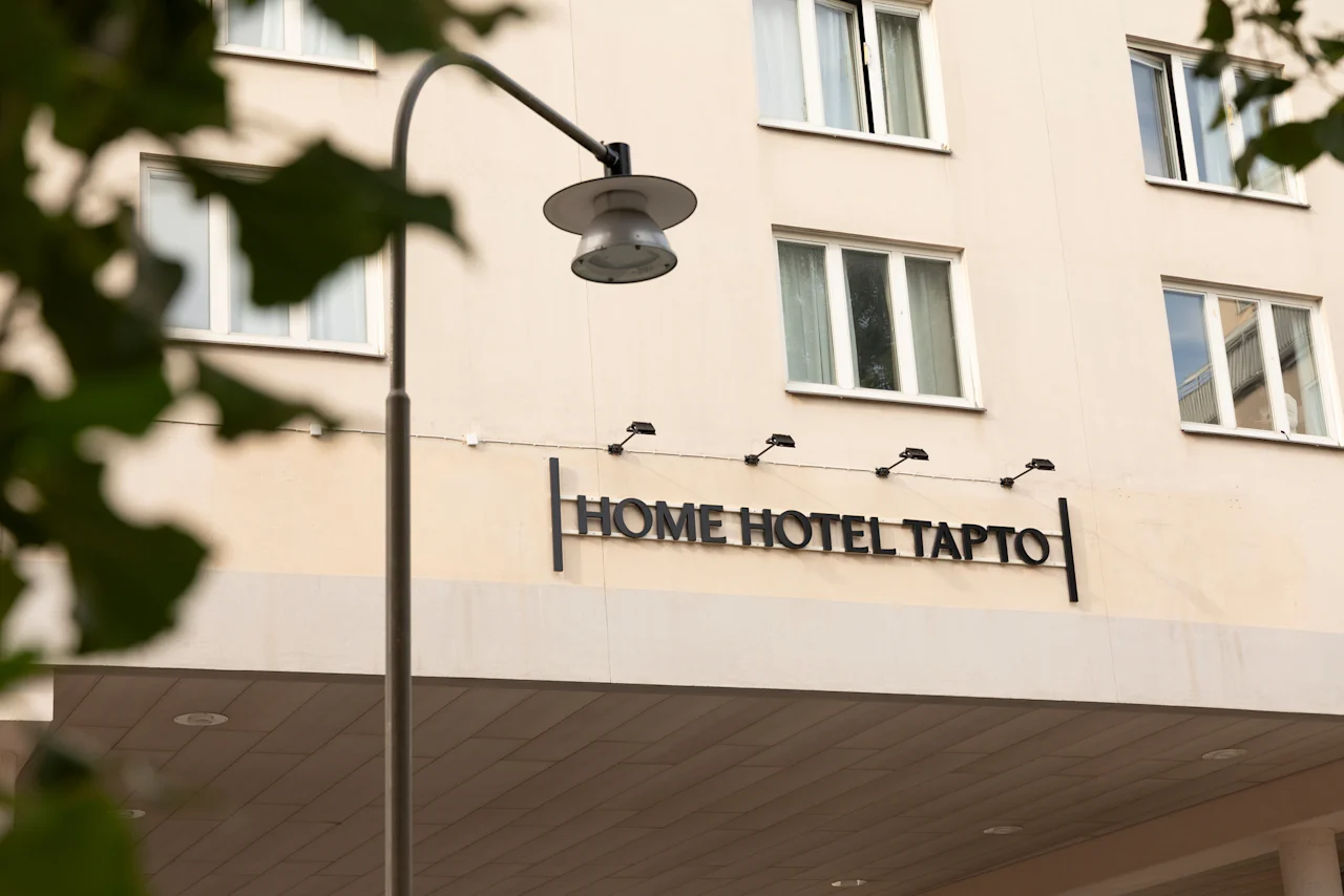 The exterior of a building with a sign that reads HOME HOTEL TAPTO, with a street lamp in the foreground.