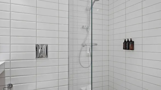 Ett rent och modernt badrum med toalett och en dusch med vita kaklade väggar och ett klinkergolv.