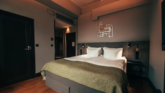 A modern hotel room with a large bed, dark walls, and warm lighting, creating a cozy atmosphere.
