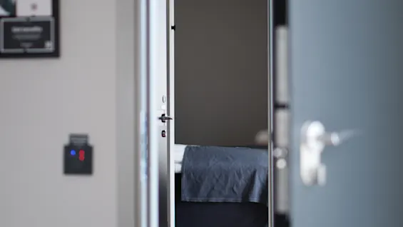 En delvis åpen dør gir et glimt inn i et hotellrom med en oppredd seng og en kortleser på veggen.