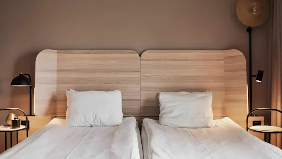 Två bekväma sängar med vita lakan och sänggavlar i trä i ett modernt hotellrum.