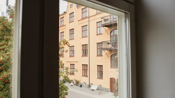 View from a window looking out at a charming building with balconies and a courtyard with benches and trees. Home Hotel Uppsala.