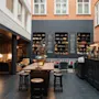 En varm og indbydende hotellounge med bar, fællesbord og siddepladser. Menupunkter som VITE VIN og ROSE er synlige.