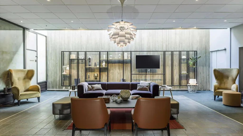 Moderne og koselig hotellobby med stilfulle lenestoler, en mørk sofa og en iøynefallende taklampe.