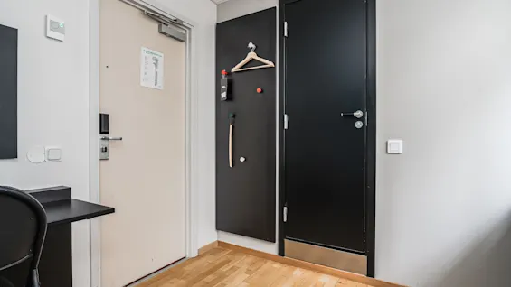 Hotel room entrance featuring a light main door, a black door, a wall hanger, and wooden parquet flooring.