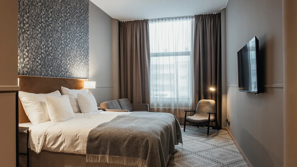 Ett modernt och inbjudande hotellrum med en bekväm säng, en mysig sittgrupp och en väggmonterad TV.