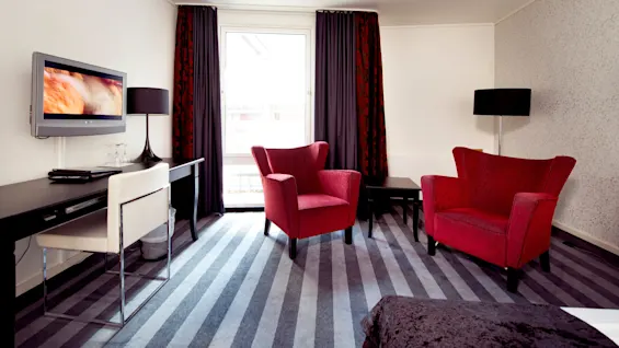 A modern room with a mounted television, black furniture, red armchairs, and striped carpeting. 