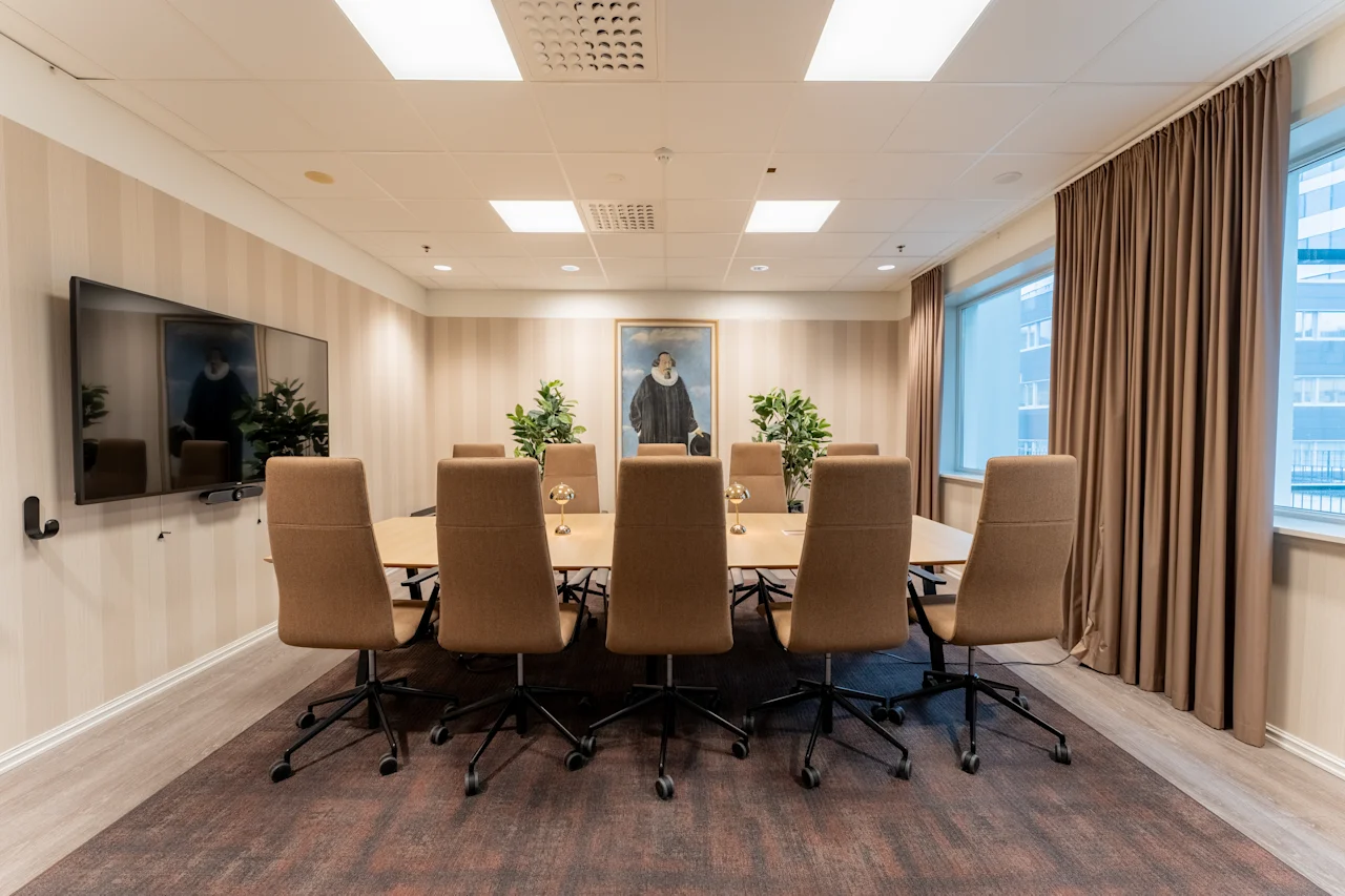 Moderni kokoushuone, jossa on pitkä pöytä, tuolit, suuri näyttö ja maalaus, valmiina tuottavaan keskusteluun.