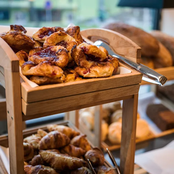 En treutstillingshylle fylt med deilige bakverk og brød, inkludert syltetøyfylte wienerbrød og sprø croissanter.