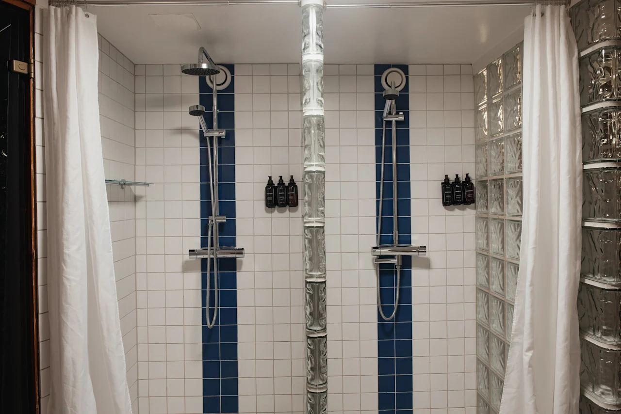 Home Hotel Kung Oscar: A clean and modern shower area with two shower heads, white and blue tiles, and glass block walls.