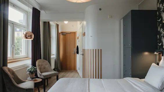 A modern hotel room with a comfortable bed, seating area, and natural light. Home Hotel Uppsala.