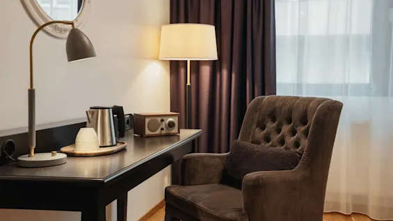 Kutsuva hotellihuoneen nurkkaus, jossa on työpöytä, virvokepiste ja mukava nojatuoli ikkunan ääressä.