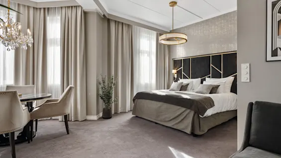 Et luksuriøst hotelværelse med en stor seng, elegant sengegavl og et hyggeligt spiseområde med en lysekrone.